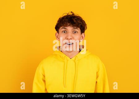 Surprised young man in yellow hoodie with wide eyes and open mouth Stock Photo