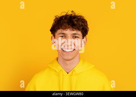 Closeup portrait of smiling young man in yellow hoodie on yellow background Stock Photo