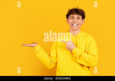 Smiling young adult man presenting open palm and pointing toward copy space Stock Photo