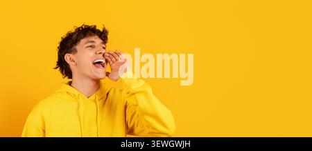 Excited young guy in yellow hoodie shouting toward empty space Stock Photo