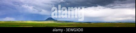 Dramatic sky over green meadow and distant hill. Clouds form dark, moody atmosphere. Grass grows tall, lush, and vibrant Stock Photo