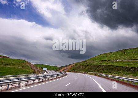 Curved highway winds through green hills under dramatic clouds Stock Photo