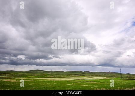 Gray clouds loom over green rolling hills. Sparse grass covers the open field Stock Photo