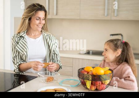 Mother preparing healthy lunchbox while talking with daughter in modern kitchen Stock Photo