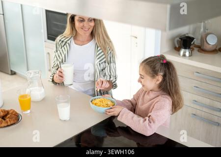 Mother and daughter enjoying healthy breakfast together in modern home kitchen Stock Photo