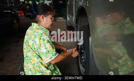 Senior asian woman mechanic removing car tire using an impact wrench Stock Photo