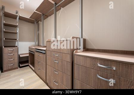 Empty luxury dressing room with walnut wood storage furniture, drawer units, shelves and metal hanging rods, modern home interior design Stock Photo