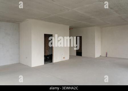 Empty unfinished apartment interior with plastered walls, concrete ceiling and floor in new residential building under construction Stock Photo