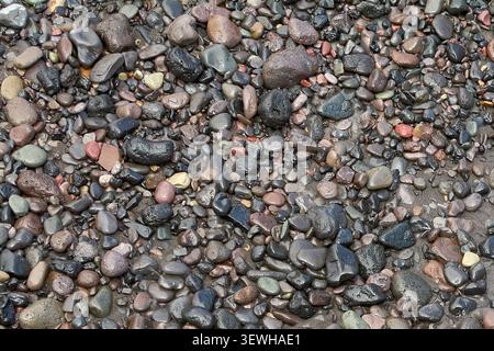 Natural texture background featuring a variety of multi-colored coastal stones and volcanic rocks. Stock Photo