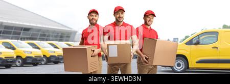 Delivery men in red uniforms holding cardboard boxes in front of cargo vans Stock Photo