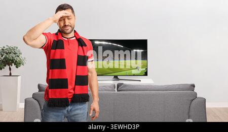 Disappointed soccer fan holding hand on forehead in front of a tv Stock Photo