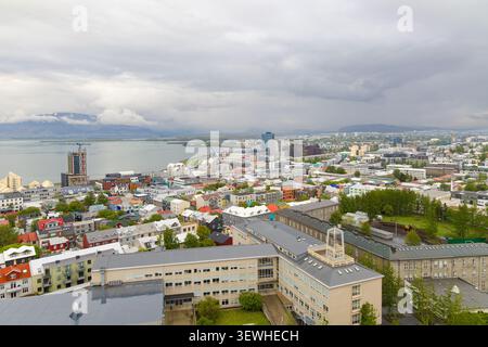 Elevated view of Reykjavik, Iceland, showing the coastal cityscape with colorful houses, institutional buildings, and mountains under a cloudy sky. Stock Photo