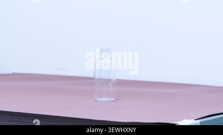 Clear plastic bottle positioned on a pink surface against a white wall, ideal for product photography and packaging design concepts Stock Photo