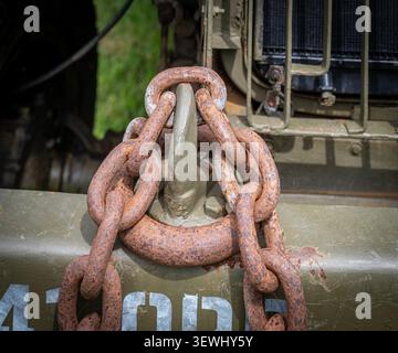 Heavy-duty, rusted tow chains and a hook attached to the front bumper of a military vehicle characteristic of vintage army trucks. Stock Photo