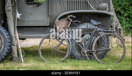This vintage black bicycle with a wicker basket and classic leather saddle is positioned against a US Army Jeep. Stock Photo