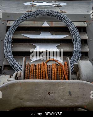 A US military vehicle with a coil of barbed wire and rusty metal cable coiled up on the vehicle's winch system. Stock Photo