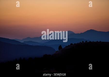 Rolling mountain peaks silhouetted against an atmospheric gradient sky at dusk Stock Photo