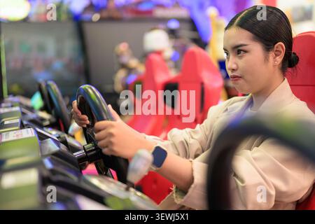 A side profile portrait of an intense young Southeast Asian Thai businesswoman from the Isan region holding an arcade steering wheel firmly with both Stock Photo