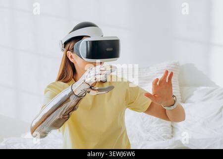 Woman wearing a vr headset and a shiny bionic prosthetic arm interacts with a virtual environment, exploring new possibilities in technology and disability inclusion Stock Photo