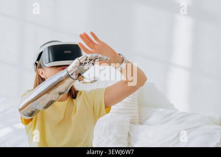 Woman wearing a virtual reality headset and bionic prosthetic arm, reaching out to interact with an immersive digital interface, exploring futuristic technology and human computer interaction Stock Photo