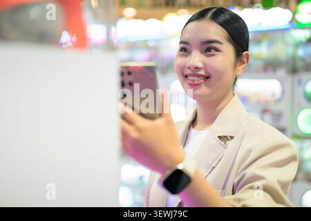 A medium horizontal portrait of a cheerful young Southeast Asian Thai businesswoman from the Isan region looking at her smartphone and smiling broadly Stock Photo