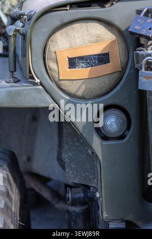 Detailed close up of a vintage olive green military vehicle featuring a fabric blackout headlight cover with a leather slit, secondary light, and heav Stock Photo