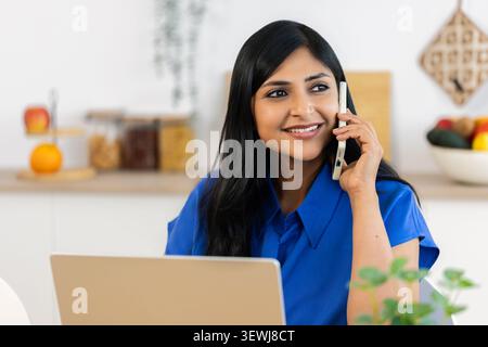 Indian woman talking on smartphone while working at home Stock Photo