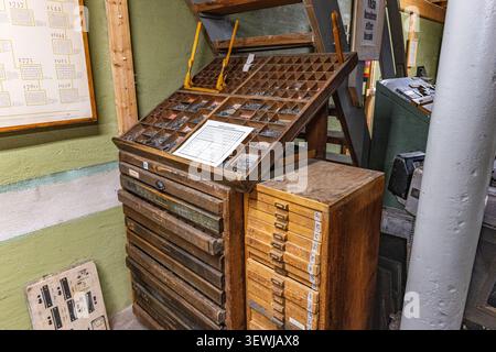 Vintage printing press stands in quiet attic space. Wooden trays hold metal type blocks for letterpress printing. Stacked drawers store aged printing Stock Photo