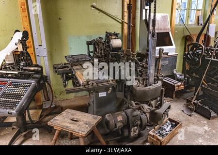 Old industrial machines cluttered a dusty workshop. Metal gears, levers, and control panels dominate the space. Tools and crates lie scattered on the Stock Photo