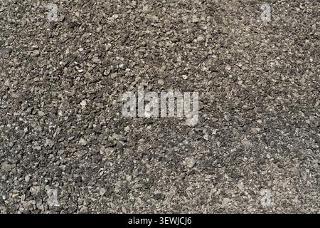 A full-frame top-down close-up view of crushed asphalt and grey stone gravel texture, showcasing a rough granular surface used as material for road co Stock Photo