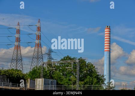 Industrial and infrastructural panorama captured on a clear day. On the left side, two large high-voltage pylons stand out, characterized by alternati Stock Photo