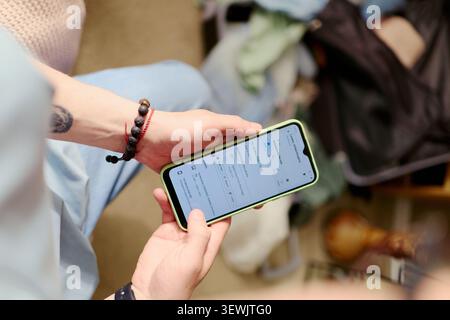 Young woman checking smartphone travel booking while packing for vacation, planning trip logistics and departure. Useful for tourism marketing, travel apps, holiday planning Stock Photo