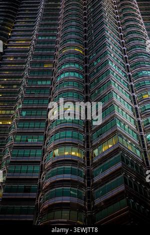 The image captures a detailed upward view of the Petronas Towers' curved facade, composed of dark gray frames, reflective green glass panels, and hori Stock Photo