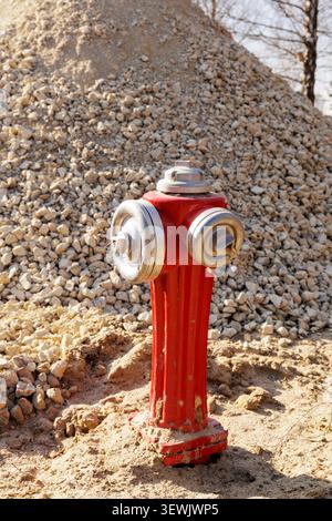 Industrial red fire hydrant standing in sand with a massive gravel heap background at a utility construction area. Stock Photo