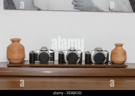 Three old analog or film cameras without lenses between two Mexican terracotta vases on a wooden dresser, traditional photographic devices that captur Stock Photo