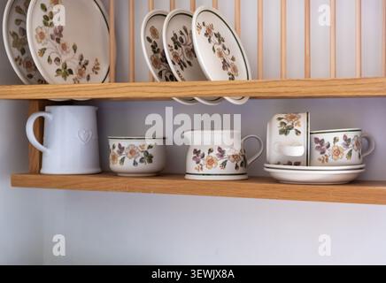 Decorative ceramic crockery displayed on a rustic wooden rack in a traditional kitchen, showcasing handcrafted patterns and warm, homely charm. Stock Photo