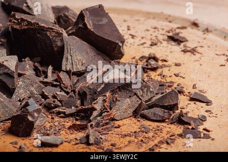 A close-up view of broken dark chocolate pieces and fine crumbs spread across a light-colored wooden board, highlighting the texture and deep color Stock Photo