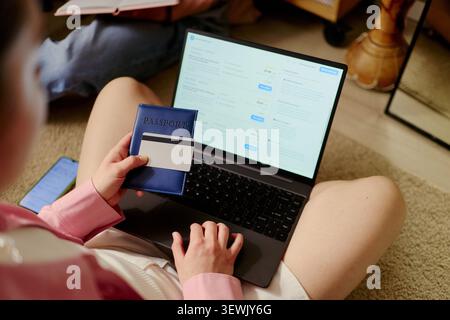Young adult couple preparing for vacation, booking travel on laptop while holding passport and bank card. Ideal for tourism marketing, trip planning, online booking services Stock Photo