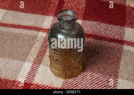 A small, decorative glass bottle with raised circular designs and a textured surface rests on a cozy, checkered fabric Stock Photo