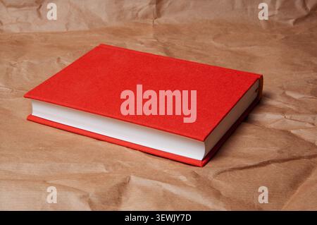 A simple, elegant red book with crisp white pages lies on crumpled brown paper, creating a minimalist composition Stock Photo