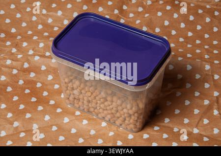 Clear plastic container filled with dried chickpeas on a brown paper with white hearts Stock Photo