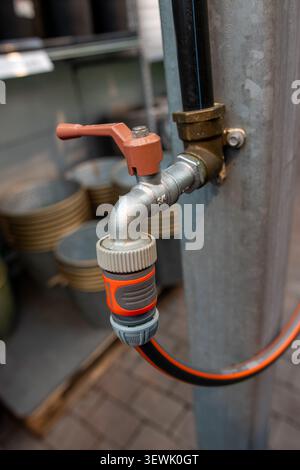 Orange handle grips metal pipe attached to gray pole. Black hose wraps around pipe with bright orange connector. Toolbox background suggests work or r Stock Photo