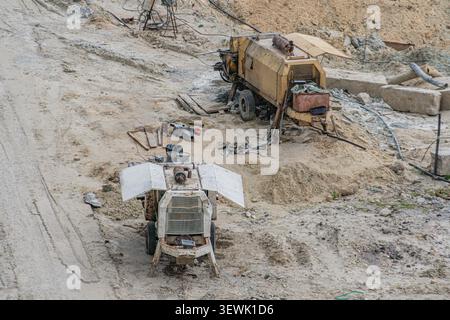 Industrial construction site featuring two large mixing machines, one white and rusted, the other yellowish-brown, surrounded by dirt, rocks, wood, me Stock Photo