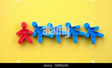 One red plastic figure standing apart in a row of blue plastic figures on a yellow background, symbolizing individuality, unique identity, and leaders Stock Photo