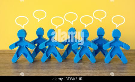 Group of blue plastic figures arranged in a row with white drawn speech bubbles above their heads on a wooden surface and yellow background, depicting Stock Photo