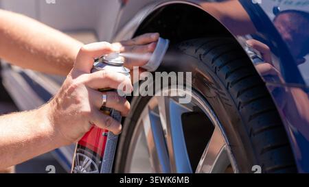 Close up of hands applying tire shine spray and foam applicator to a car tire during professional auto detailing and vehicle maintenance. Stock Photo