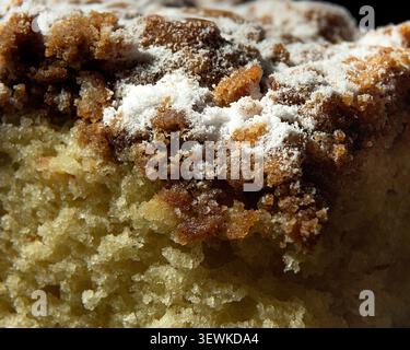 Close-up macro photograph of a moist coffee crumb cake slice topped with crunchy streusel and a dusting of powdered sugar, emphasizing golden-brown ba Stock Photo