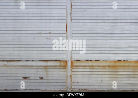 Rusty Metal Gate Background. Old white corrugated metal gate with rust stains and weathered industrial texture. Stock Photo