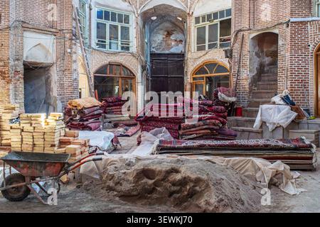 Shot in a courtyard of the Tabriz Bazaar. The foreground features a pile of sand, a wheelbarrow, and stacks of construction bricks, while the backgrou Stock Photo