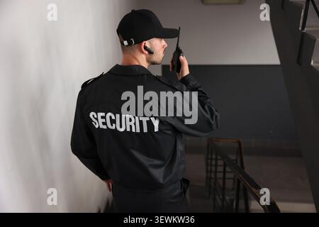 Bodyguard in uniform using walkie talkie while walking down stairs indoors Stock Photo